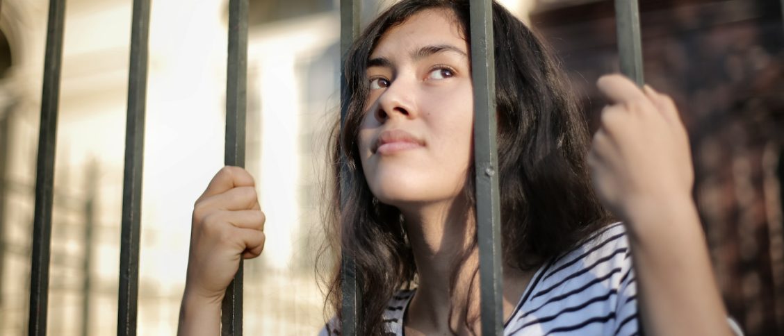 Sad isolated young woman looking away through fence with hope