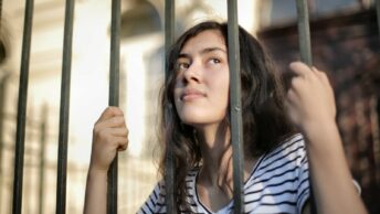 Sad isolated young woman looking away through fence with hope