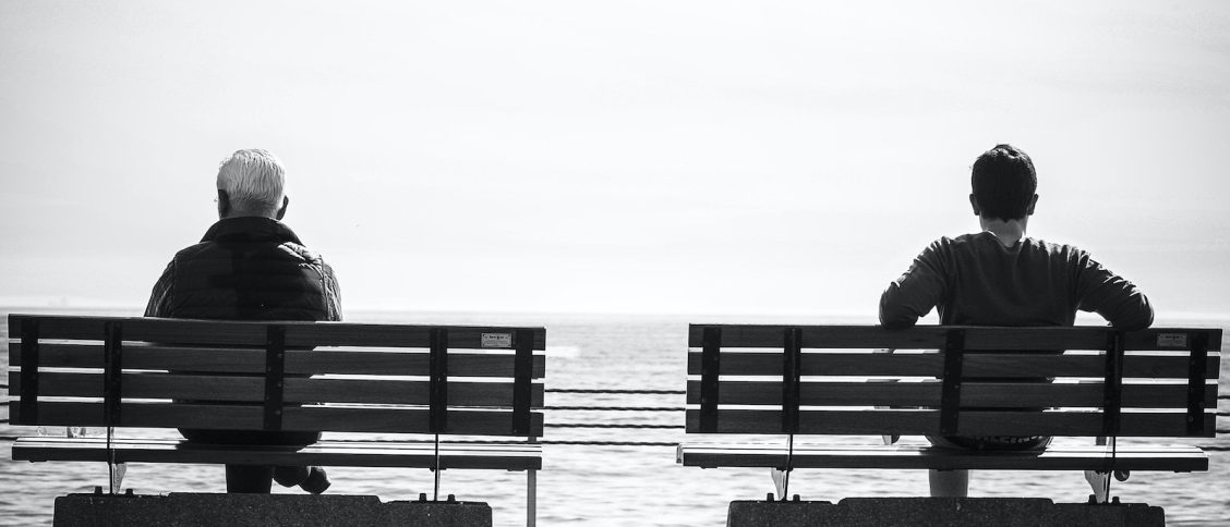 Grayscale Photo 2 Person Sitting in a Separate Benches on the Seaside