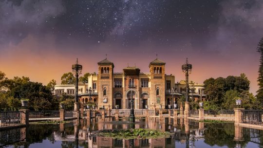 a large building sitting on top of a lake under a night sky