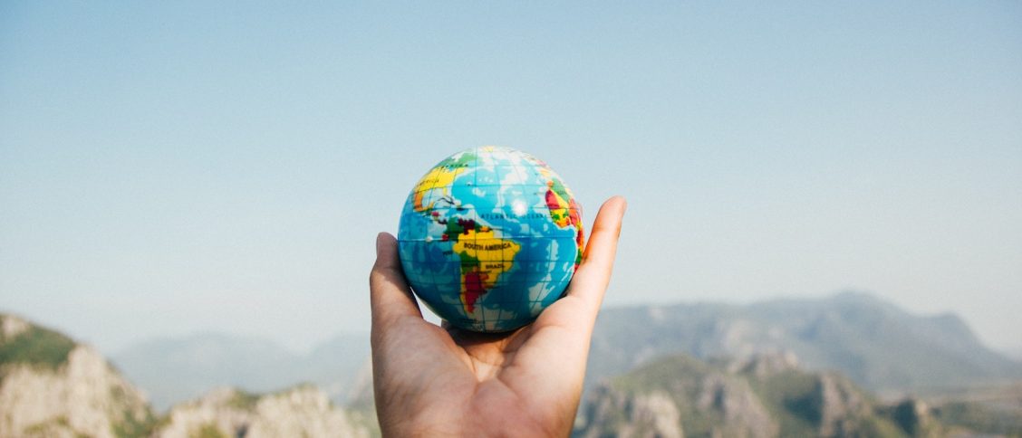 Person Holding World Globe Facing Mountain