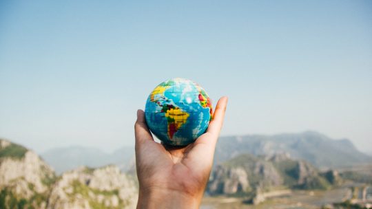 Person Holding World Globe Facing Mountain