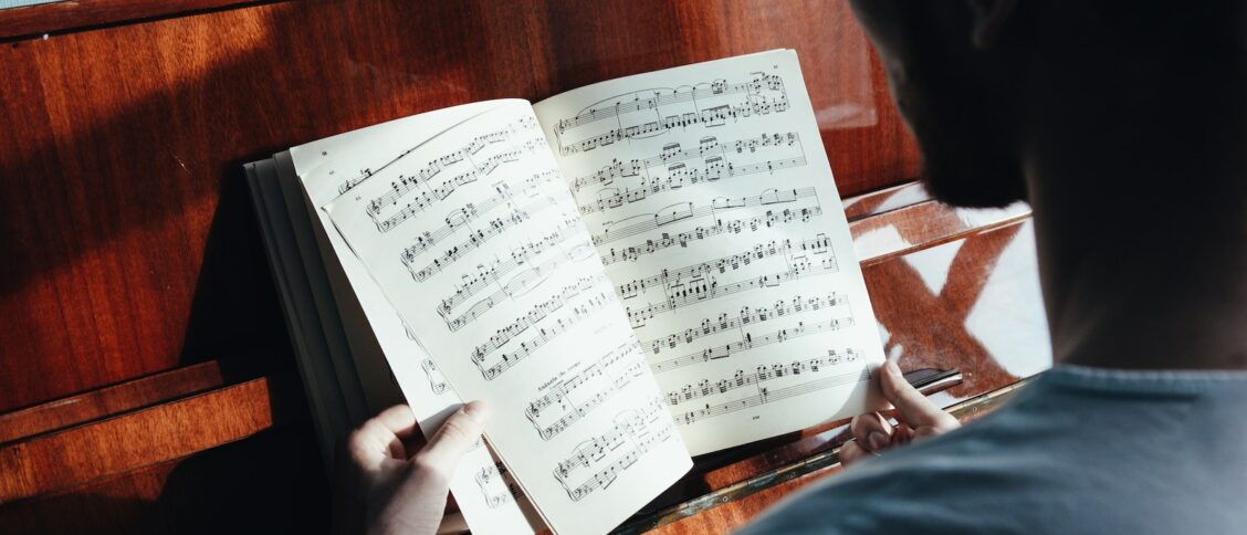 Back view of crop anonymous male pianist watching music paper with written notes near piano