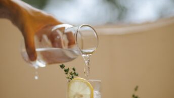 Crop person pouring water in lemonade