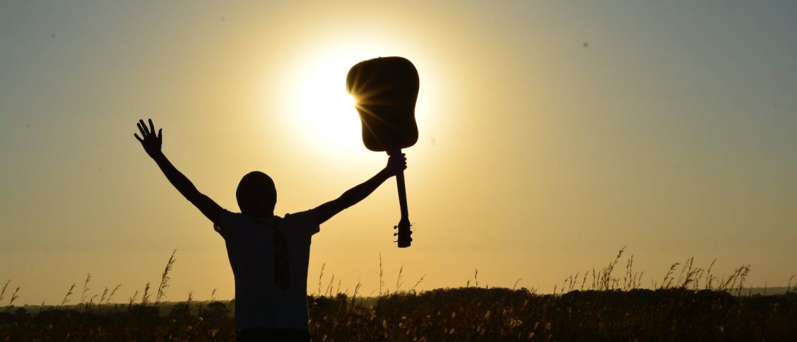 Silhouette of Man Holding Guitar on Plant Fields at Daytime